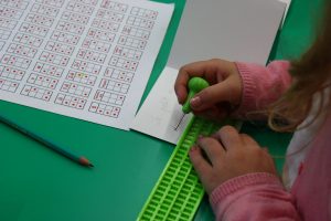 gros plan sur des mains d'enfant qui écrivent en braille sur un mini livre
