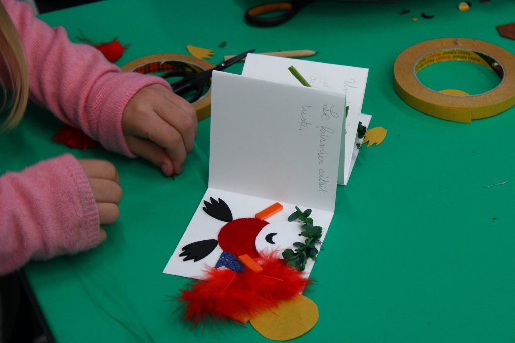 Un mini livre avec une phrase écrite d'une écriture d'enfant et une illustration faite en collage de matières. Des mains d'enfants tournent les pages
