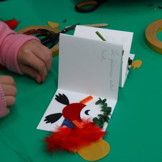 Un mini livre avec une phrase écrite d'une écriture d'enfant et une illustration faite en collage de matières. Des mains d'enfants tournent les pages