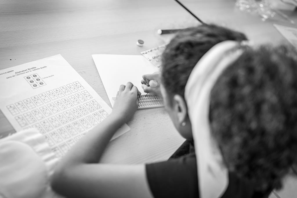 Une petite fille écrit en braille avec un poinçon et une tablette, ainsi qu'un alphabet braille.
