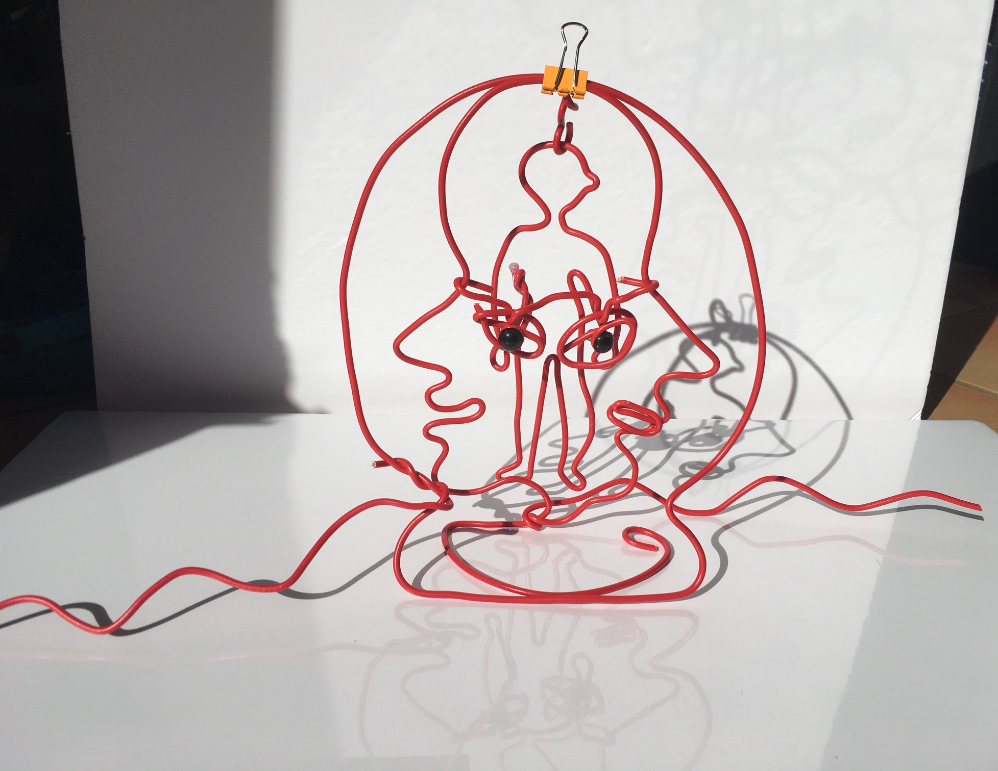 En fil de fer rouge, adaptation tactile de l'autoportrait de Louise Bourgeois (silhouette d'une personne superposée sur un visage)