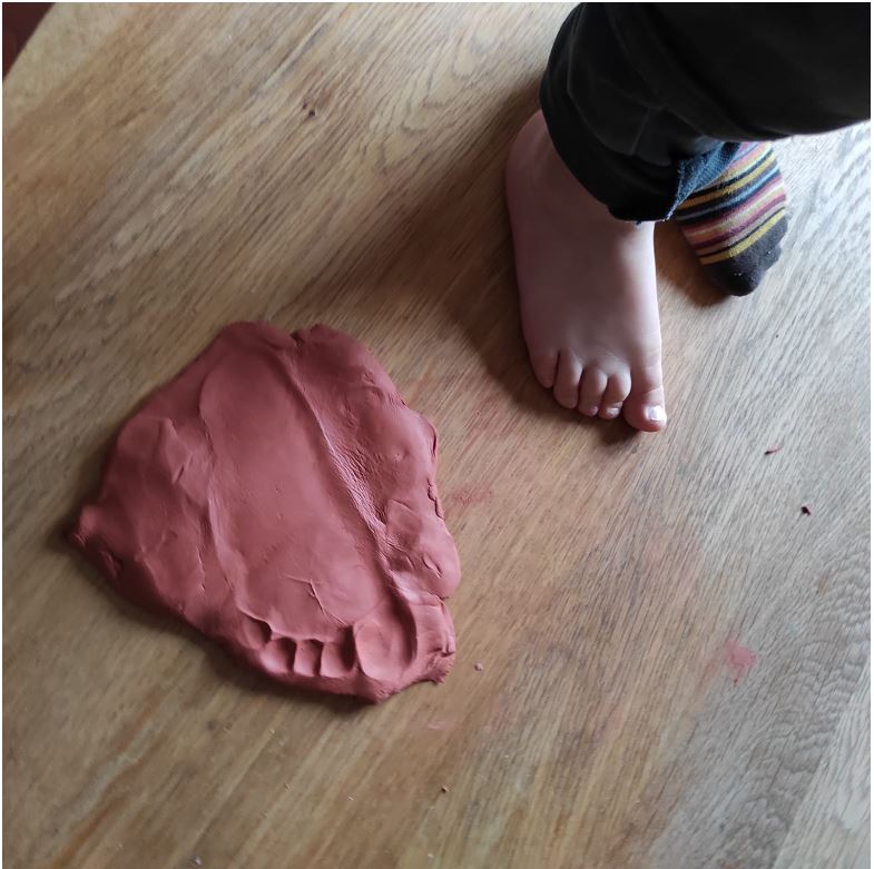 Photo d'un pied d'enfant à côté de son empreinte dans de la pâte durcissante