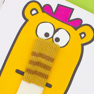 gros plan sur l'illustration tactile de la chuassettes rayée à la place du nez du personnage, le personnage est jaune orangé et en flocage doux au toucher, il a un chapeau rose sur la tête