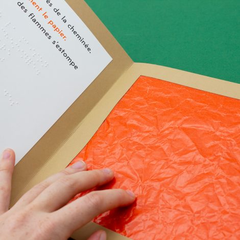 une main effleure papier sulfurisé orange, texte en noir et braille