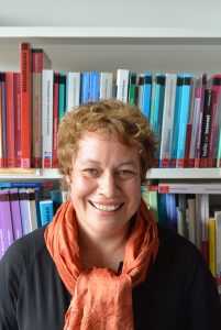 Agnès Bergonzi souriante, devant une bibliothèque de livres multicolores