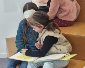 deux fillettes lisent un livre tactile. L'une a un bandeau sur les yeux