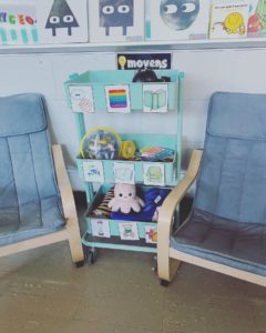 photo d'un "coin calme" dans une classe. Deux fauteuils sont placés de part et d'autre d'une étagère dans laquelle sont rangés des activités à réaliser en autonomie (on aperçoit des livres, des peluches, des jeux...)