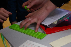 Une main s'active pour utiliser une tablette braille posée sur une table