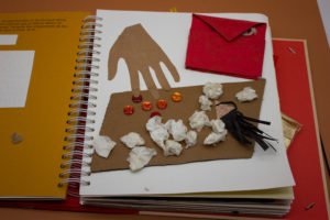 Zoom sur une illustration tactile avec une enveloppe représenté en carton, une main, une table avec des papiers chiffonnés dessus.