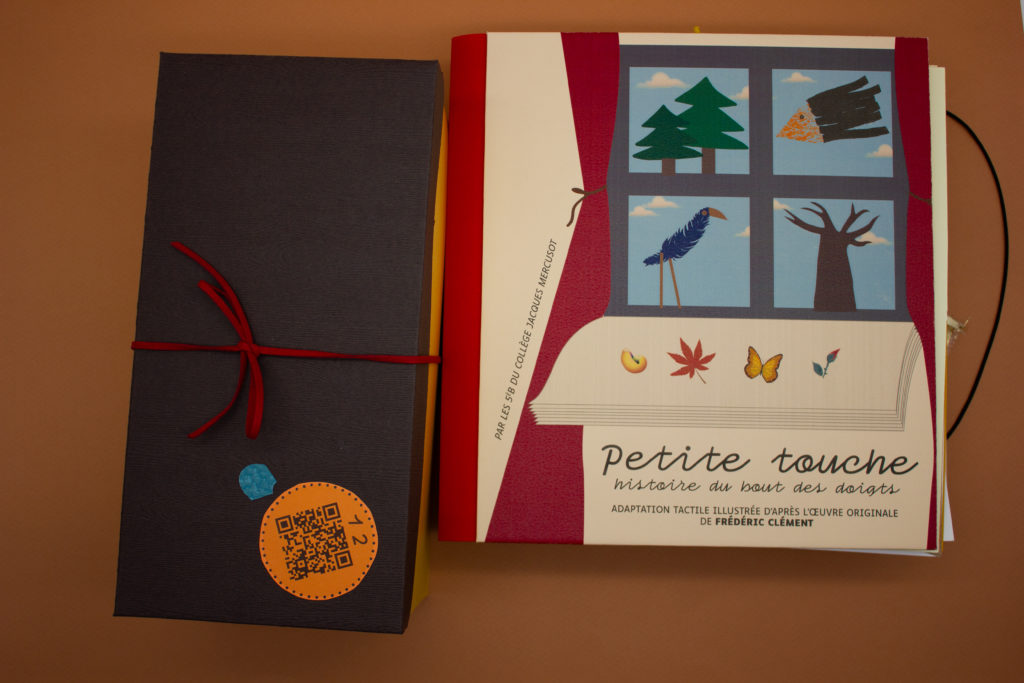 Boîte avec un QR code. La boîte est posé à côté du livre tactile. Couverture du livre tactile. On y voit une fenêtre dessinée, avec derrière la fenêtre un arbre et un oiseau.