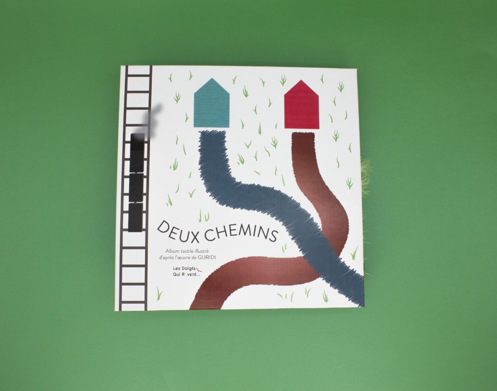 Couverture du livre tactile sur laquelle on peut voir deux chemins qui se croisent et qui partent chacun d'une maison. Sur le côté il y a des rails avec un train qui passe.