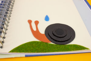 Page du livre avec une illustration tactile, un escargot qui reçoit une goutte sur lui