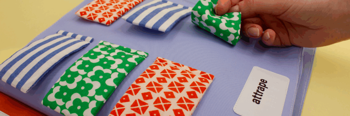 6 bouts de tissus avec une main qui attrape un bout de tissu. Attrape est écrit en grand caractère et en braille.