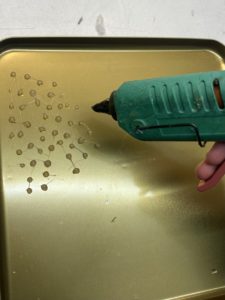Photo d'un couvercle en métal sur lequel est déposé des petites gouttes de colle avec un pistolet à colle chaude.