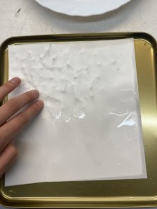 Photo d'une main qui appuie sur une feuille mouillée posée sur un couvercle en métal. Des reliefs apparaissent sur la feuille.