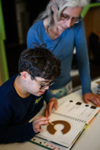 Un enfant en situation de handicap assite d'une educatrice specialisee manipule un ouvrage illustre en braille