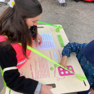 Camille notre animatrice qui déambule dans les rues avec le brailleur ambulant et un enfant essaye d'écrire en braille sur le plateau qu'elle porte